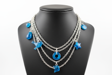 Load image into Gallery viewer, a necklace of silver chains with blue colored charms on a black jewelry display with a white background