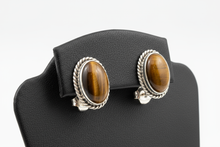 Load image into Gallery viewer, a pair of silver post back earrings with a BROWN stone on a black faux leather jewelry display with a white background