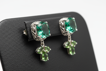 Load image into Gallery viewer, a pair of silver post back earrings with a GREEN stone on a black faux leather jewelry display with a white background
