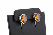 Load image into Gallery viewer, a pair of silver post back earrings with a ORANGE stone on a black faux leather jewelry display with a white background
