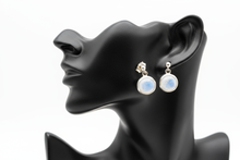 Load image into Gallery viewer, a pair of silver post back earrings with a white stone on a black faux leather jewelry display with a white background
