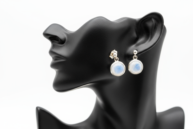 a pair of silver post back earrings with a white stone on a black faux leather jewelry display with a white background