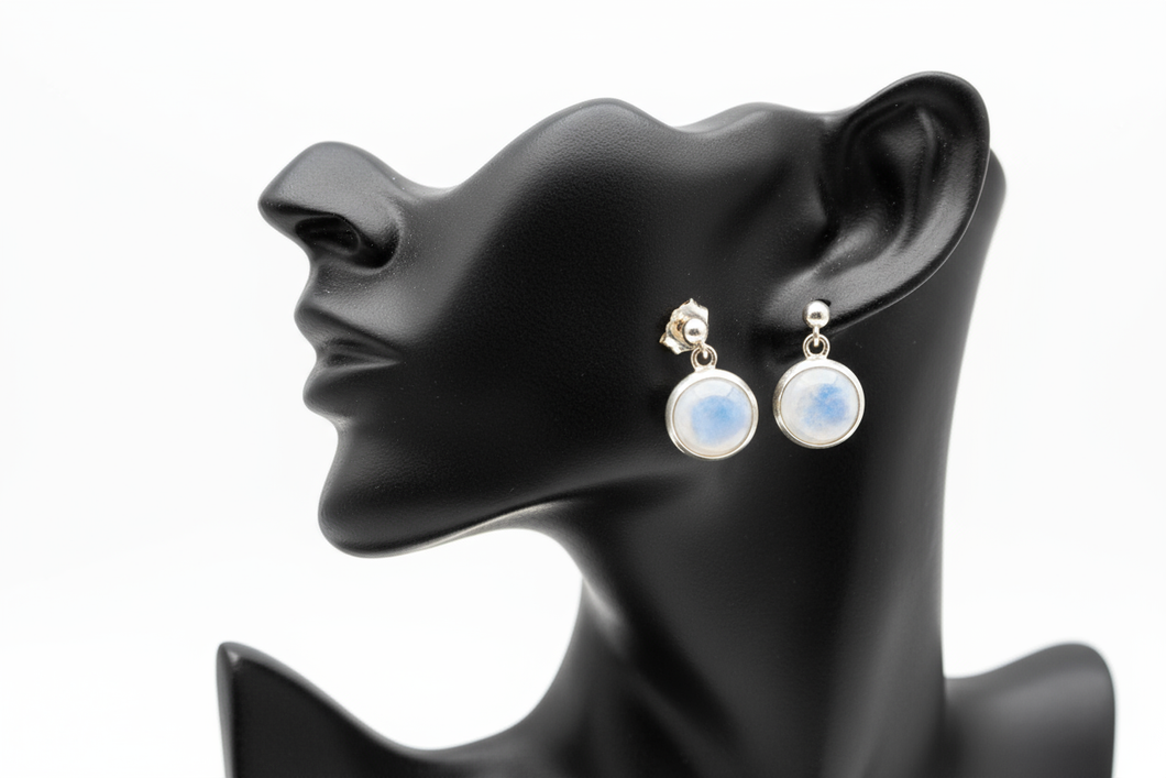 a pair of silver post back earrings with a white stone on a black faux leather jewelry display with a white background