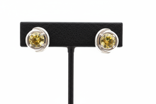 Load image into Gallery viewer, a pair of silver post back earrings with a yellow stone on a black faux leather jewelry display with a white background
